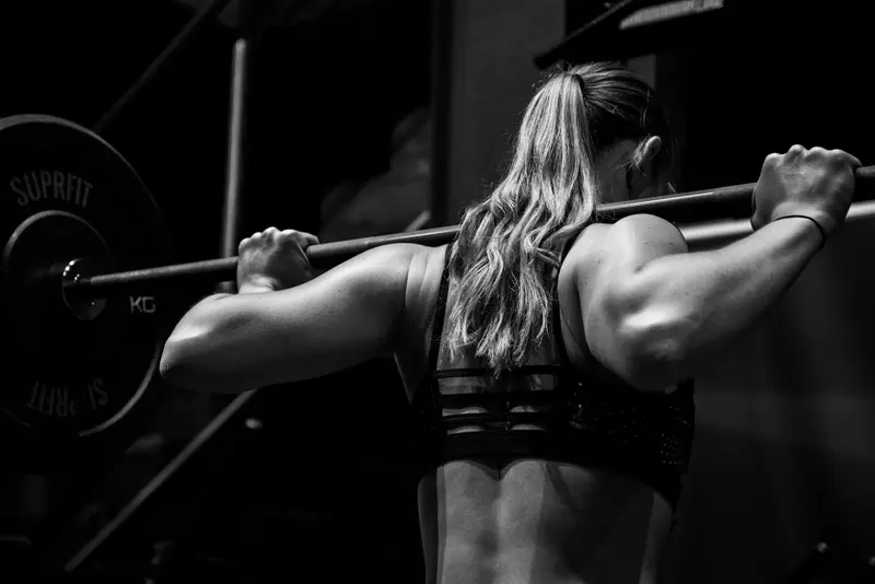 Entrenadora de espaldas sujetando una barra en el gimnasio