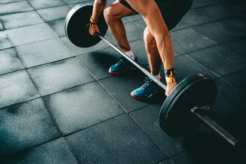 Piernas de un atleta junto a una barra con discos